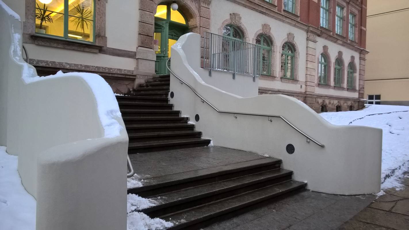 Edelstahlhandlauf parallel zur geschwungenen Betonwand am Eingang der Ludwig Richter Grundschule