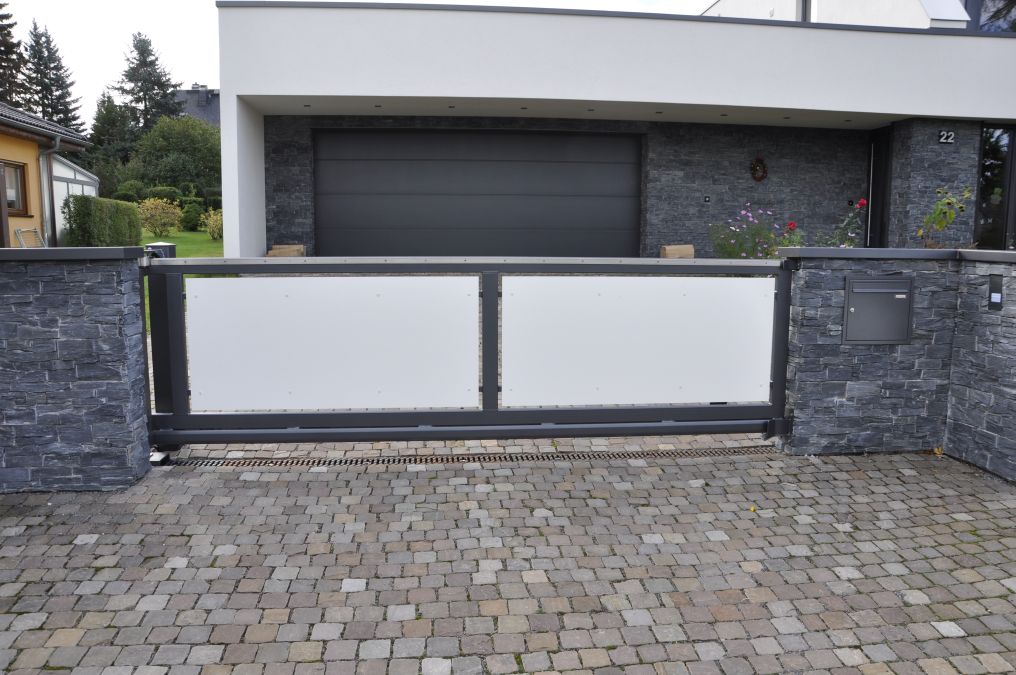 Automatisierte Schiebetoranlage mit Eingangspforte und Briefkasten. Füllung der Tore aus HPL – Platten