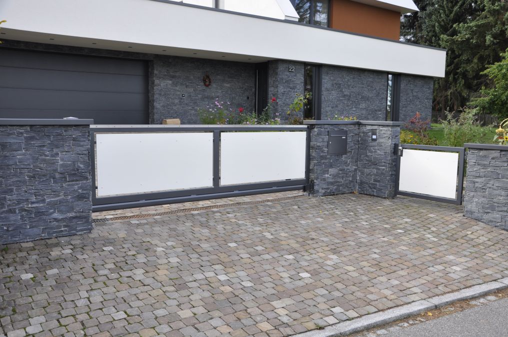 Automatisierte Schiebetoranlage mit Eingangspforte und Briefkasten. Füllung der Tore aus HPL – Platten